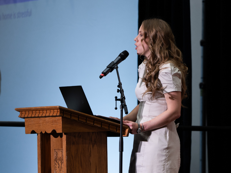 A woman stands confidently at a podium, addressing an audience.